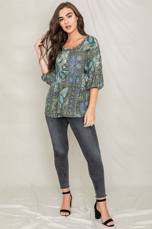 A woman with long brown hair wearing the Button Accent Paisley Top in green and blue, made from polyester, stands against a plain background.
