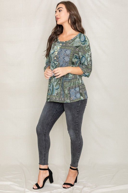 A person with curly black hair wears the Plus Button Accent Paisley Top paired with black pants, standing with one hand behind their head.