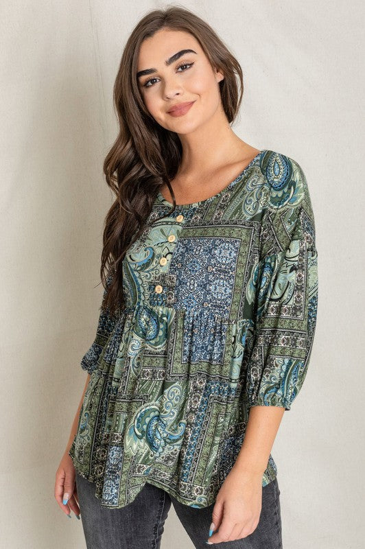 A woman with long brown hair wearing the Button Accent Paisley Top in green and blue, made from polyester, stands against a plain background.