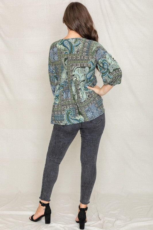 A woman with long brown hair wearing the Button Accent Paisley Top in green and blue, made from polyester, stands against a plain background.