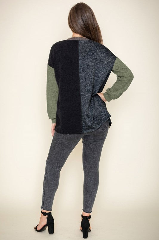 A woman is smiling and touching her hair while wearing the Color Block Knit Cardigan, featuring shades of black, grey, and beige. She has paired it with a black top and grey jeans. The cardigan is made from 95% rayon and is proudly manufactured in the United States.