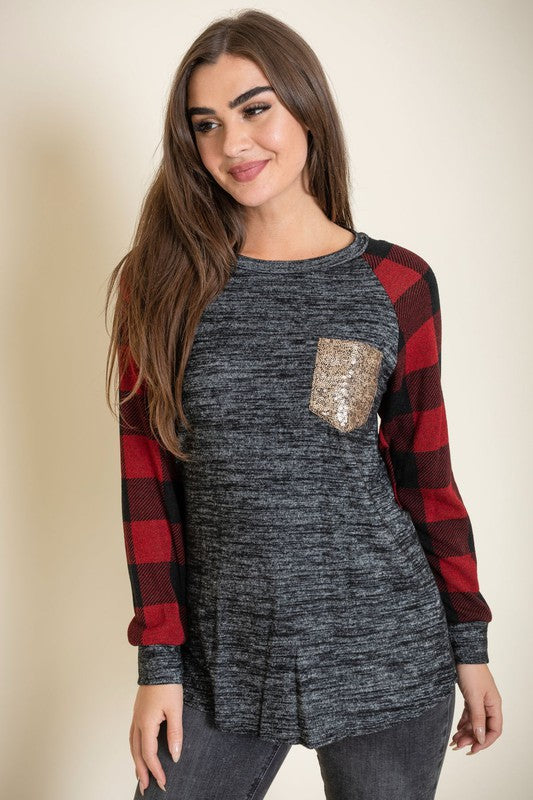 A woman with long brown hair is smiling and wearing a Checker Sleeve Sequin Pocket Tunic in black and red, featuring checker sleeves and a gold sequin pocket.