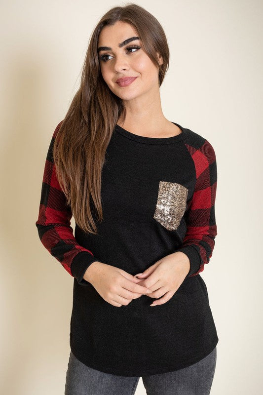 A woman with long brown hair is smiling and wearing a Checker Sleeve Sequin Pocket Tunic in black and red, featuring checker sleeves and a gold sequin pocket.