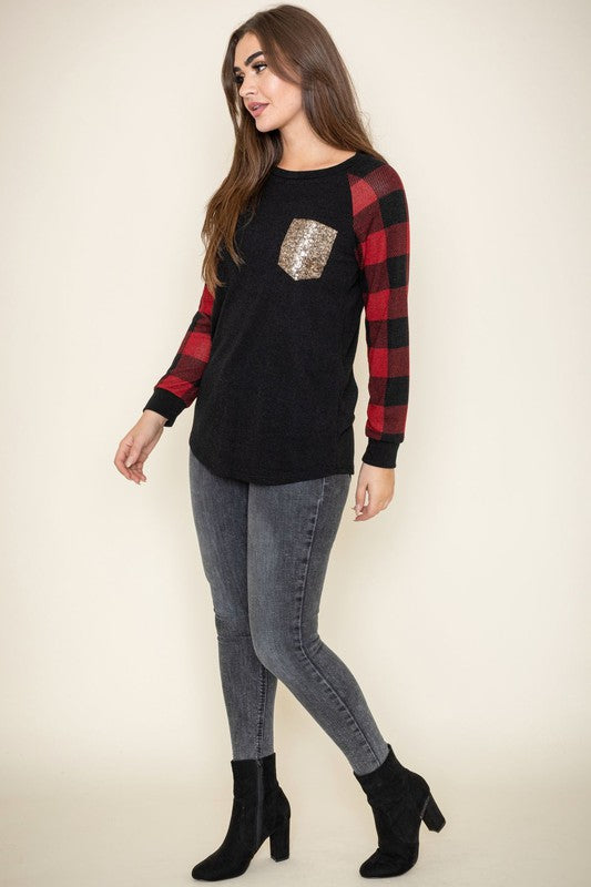 A woman with long brown hair is smiling and wearing a Checker Sleeve Sequin Pocket Tunic in black and red, featuring checker sleeves and a gold sequin pocket.