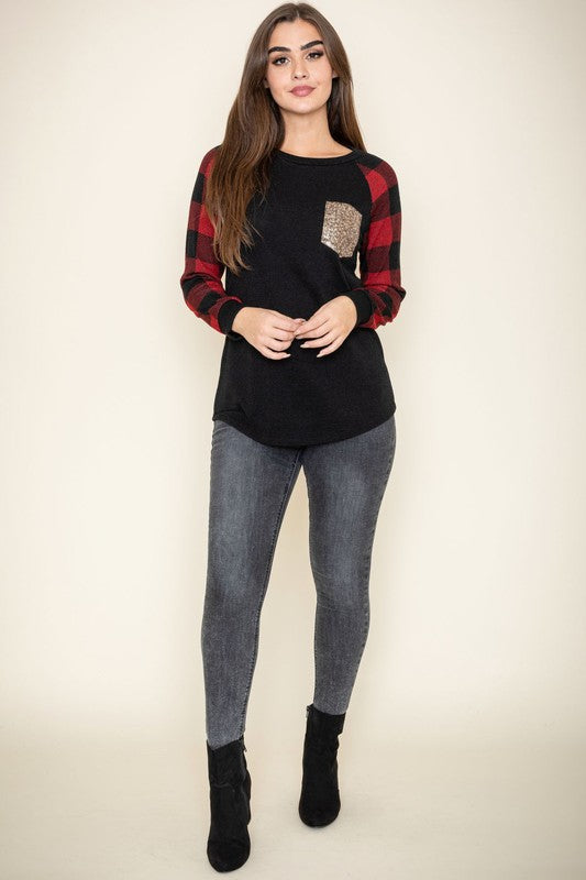 A woman with long brown hair is smiling and wearing a Checker Sleeve Sequin Pocket Tunic in black and red, featuring checker sleeves and a gold sequin pocket.