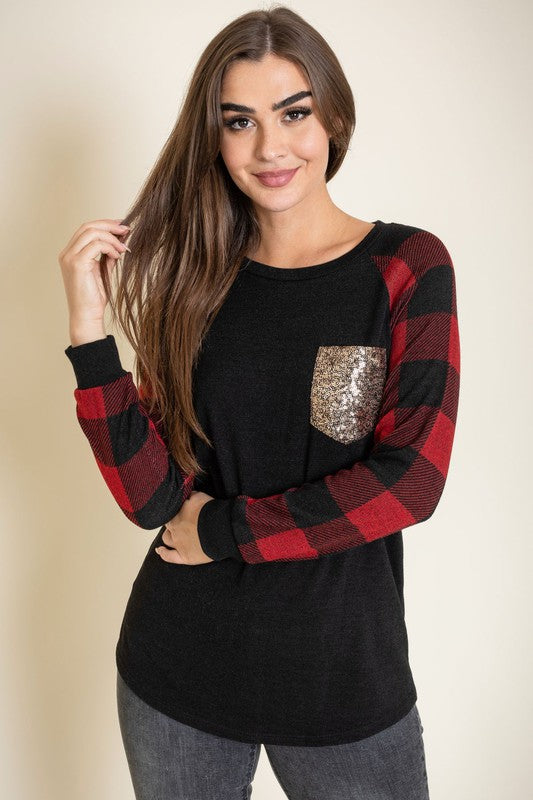 A woman with long brown hair is smiling and wearing a Checker Sleeve Sequin Pocket Tunic in black and red, featuring checker sleeves and a gold sequin pocket.