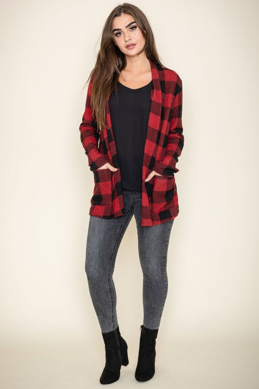 A woman stands against a plain background, wearing the Checkered Elbow Patch Cardigan with stylish elbow patches in red and black, paired with a black top, gray jeans, and black ankle boots. The ensemble captures a timeless look that's effortlessly chic.