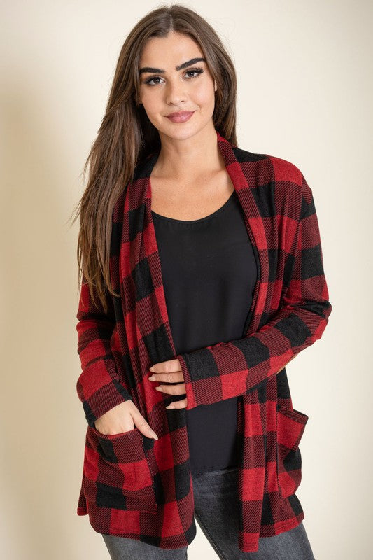 A woman stands against a plain background, wearing the Checkered Elbow Patch Cardigan with stylish elbow patches in red and black, paired with a black top, gray jeans, and black ankle boots. The ensemble captures a timeless look that's effortlessly chic.