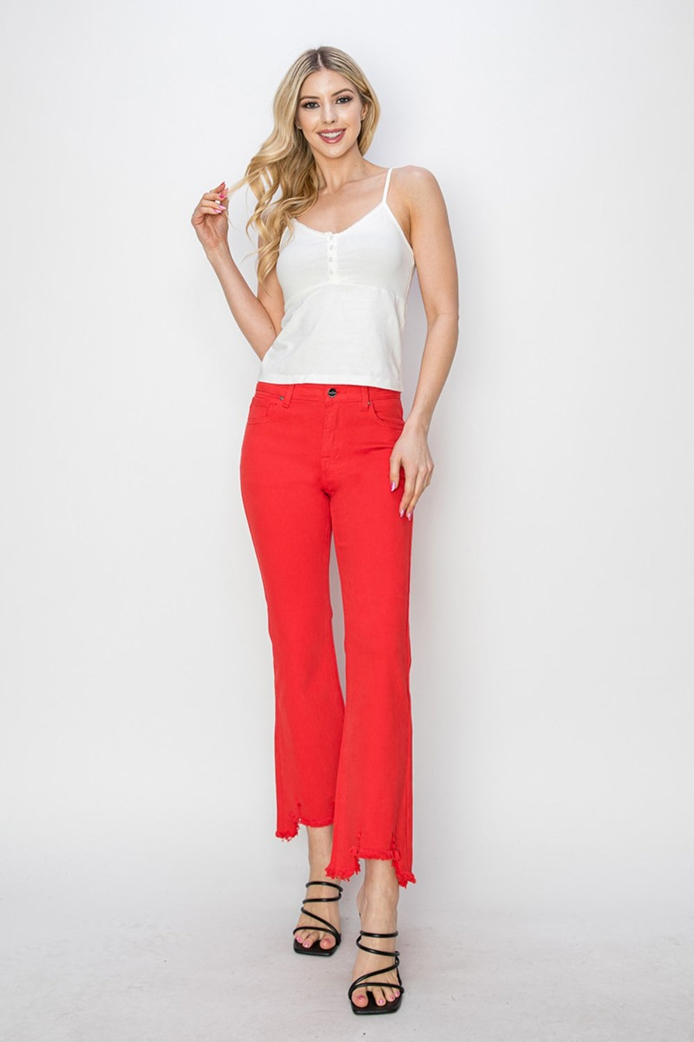 A person is wearing the RISEN Raw Hem Bootcut Jeans with Pockets in bright red, paired with a white top and black strappy high-heeled sandals. The image focuses on the stylish and functional lower half of the body.