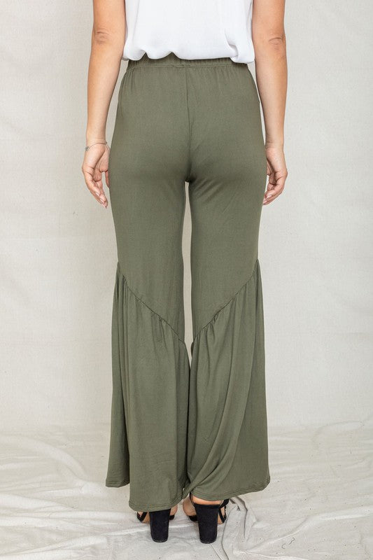 A person wearing olive green Diagonal Trim Ruffle Hem Pants with wide-leg, flared bottoms, made from a comfortable blend of rayon and spandex, stands outdoors on a paved area.
