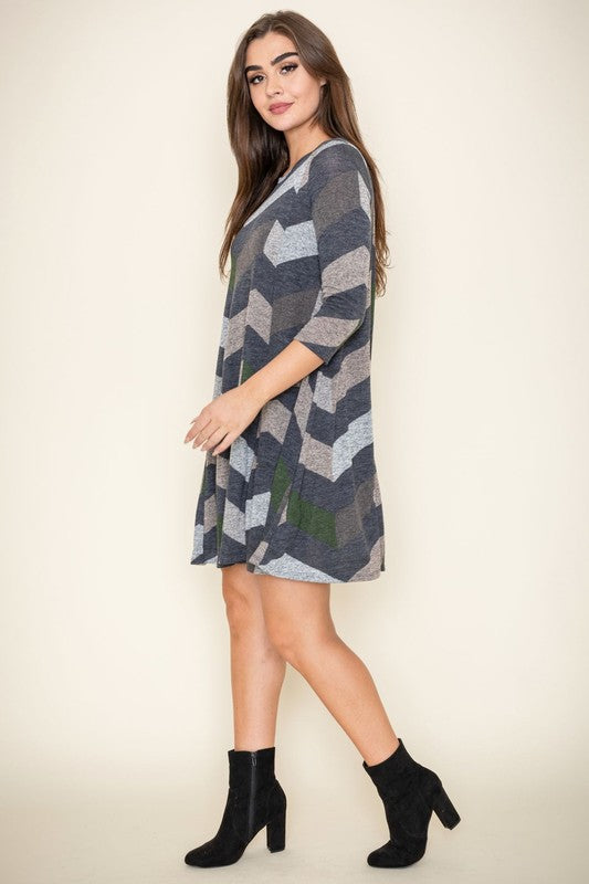 A person stands against a plain background, showcasing the Plus Chevron A-Line Dress in grey, taupe, and teal. The dress features three-quarter sleeves and is crafted from a polyester spandex blend, effortlessly combining comfort and style.