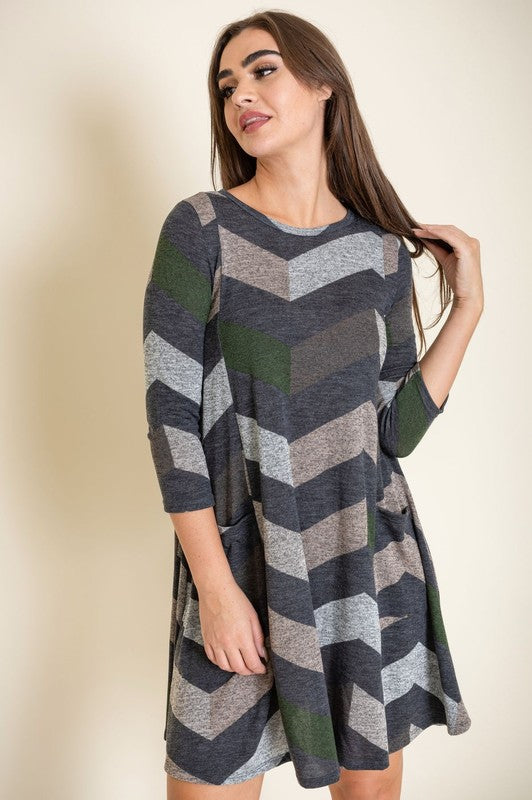 Against a plain backdrop, an individual elegantly poses in the Chevron A-Line Dress, featuring a polyester fabric and long sleeves.