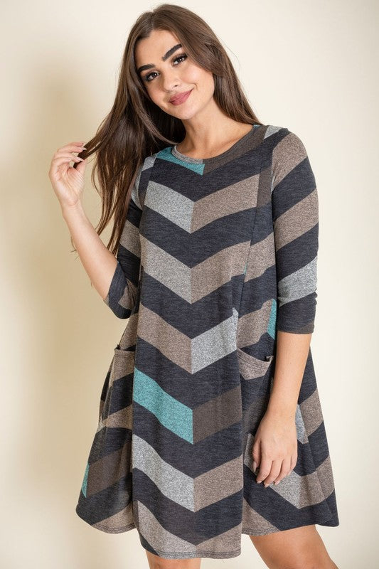 Against a plain backdrop, an individual elegantly poses in the Chevron A-Line Dress, featuring a polyester fabric and long sleeves.