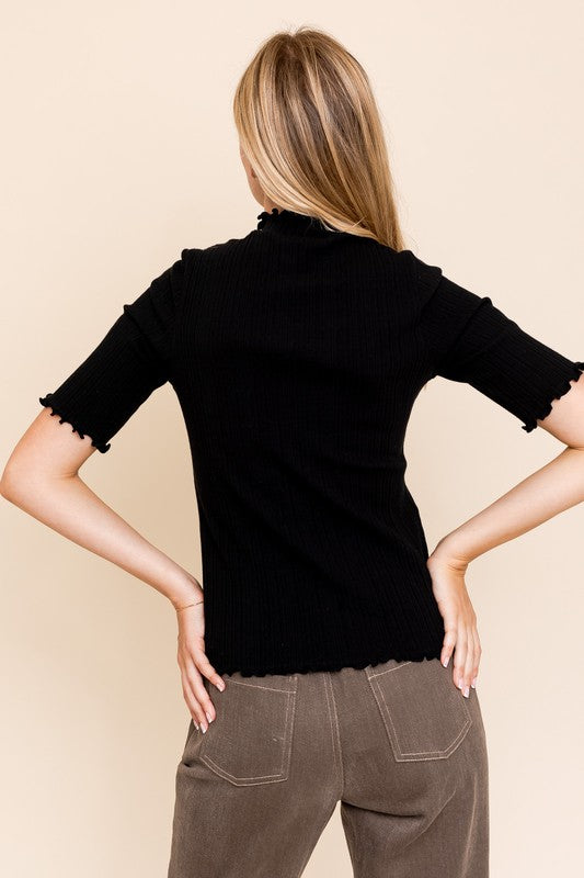 A person in a rust-colored Short Sleeve Mock Neck Merrow Edge Top holds a beige hat. They are also wearing a pleated skirt.