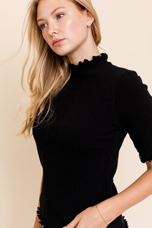 A person in a rust-colored Short Sleeve Mock Neck Merrow Edge Top holds a beige hat. They are also wearing a pleated skirt.