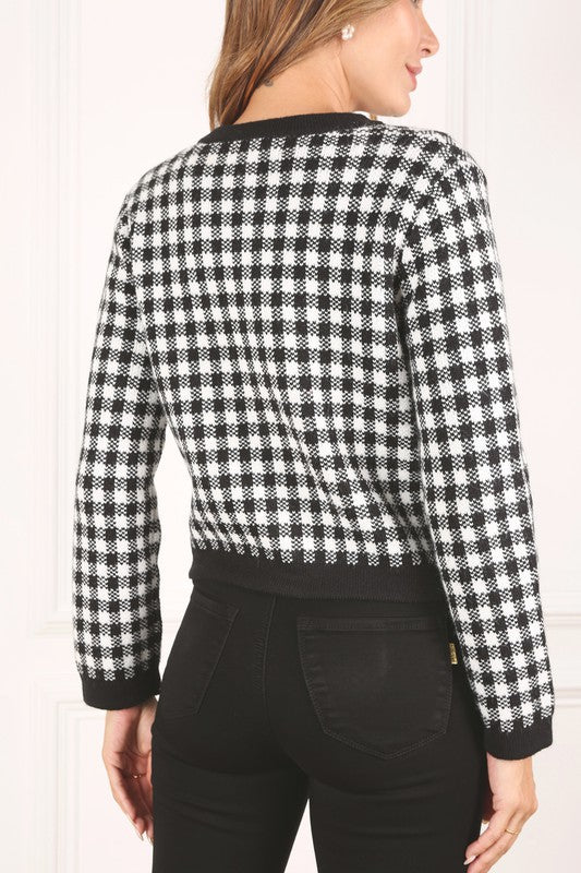 A woman dressed in the Black Check Knitted Jacket, featuring snap buttons and functional pockets, complemented by black pants, stands against a white background.