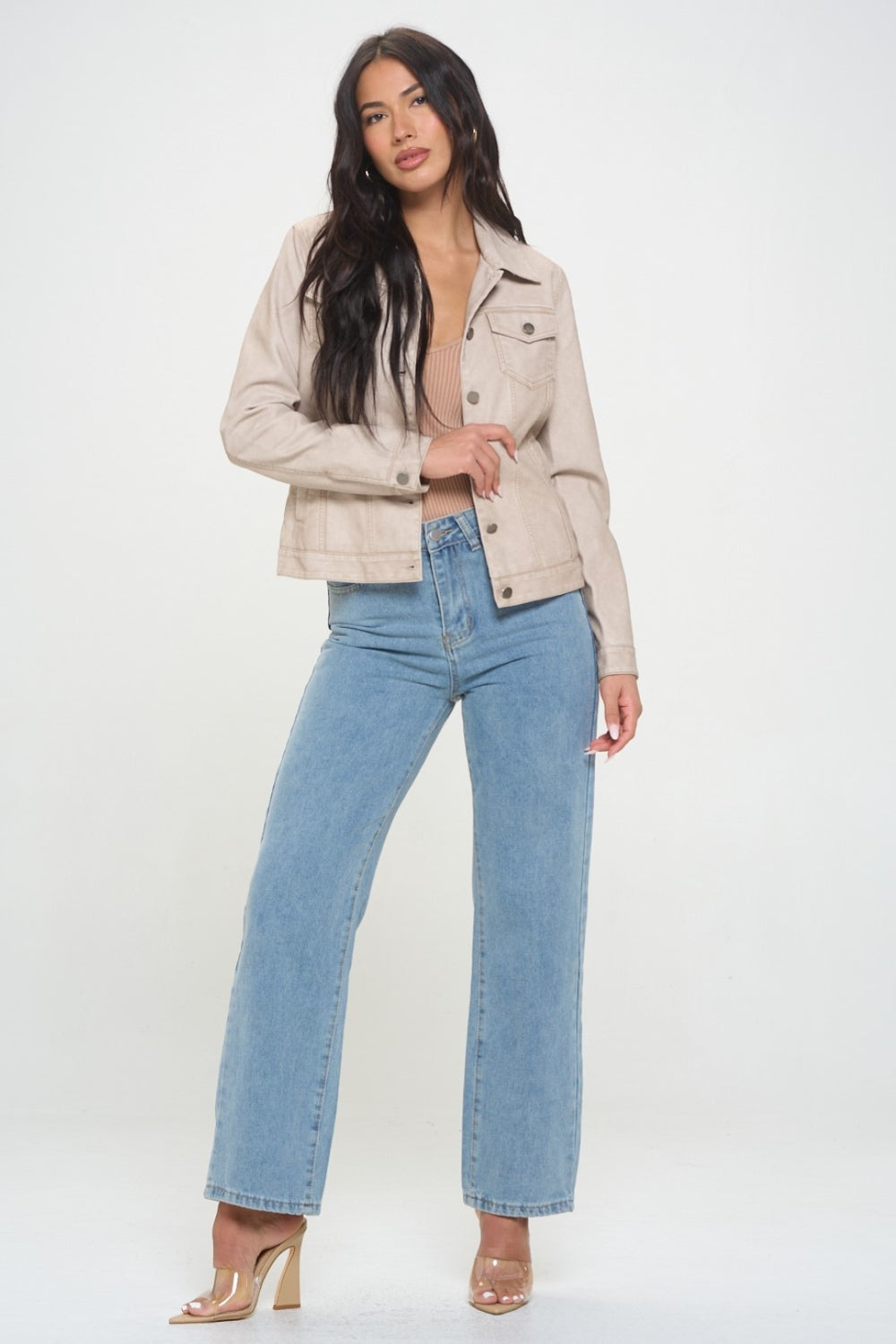 A woman with long dark hair, showcasing women's spring fashion, wears the Coalition LA Button Down Cargo Vegan Leather Shacket over a beige top and blue jeans as she stands against a plain background.