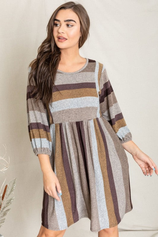 A person stands smiling, dressed in a Mix Stripe Balloon Sleeve Midi Dress that features multi-colored horizontal stripes in shades of blue, brown, and gray. The midi dress, crafted from polyester, includes three-quarter sleeves and handy pockets.