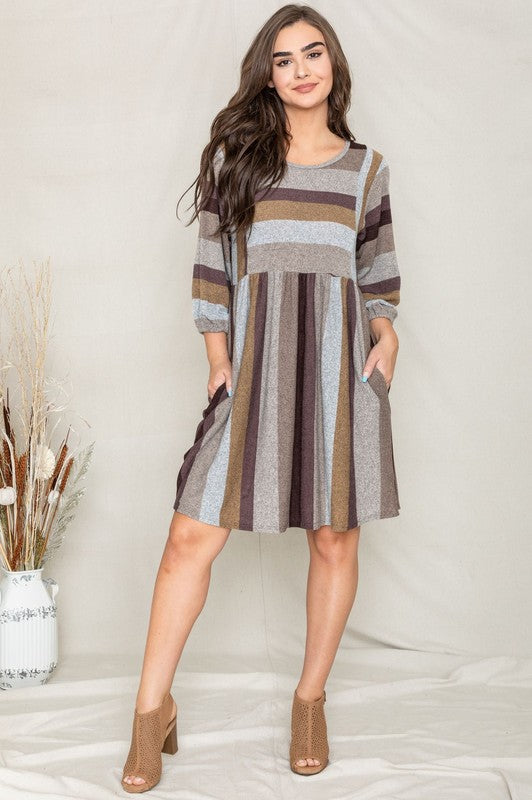 A person stands smiling, dressed in a Mix Stripe Balloon Sleeve Midi Dress that features multi-colored horizontal stripes in shades of blue, brown, and gray. The midi dress, crafted from polyester, includes three-quarter sleeves and handy pockets.