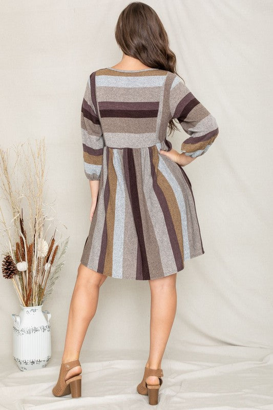 A person stands smiling, dressed in a Mix Stripe Balloon Sleeve Midi Dress that features multi-colored horizontal stripes in shades of blue, brown, and gray. The midi dress, crafted from polyester, includes three-quarter sleeves and handy pockets.