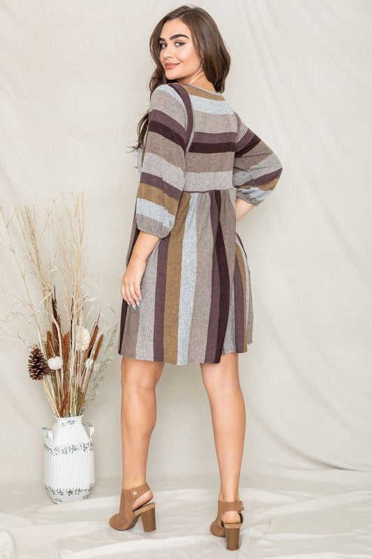 A person stands smiling, dressed in a Mix Stripe Balloon Sleeve Midi Dress that features multi-colored horizontal stripes in shades of blue, brown, and gray. The midi dress, crafted from polyester, includes three-quarter sleeves and handy pockets.