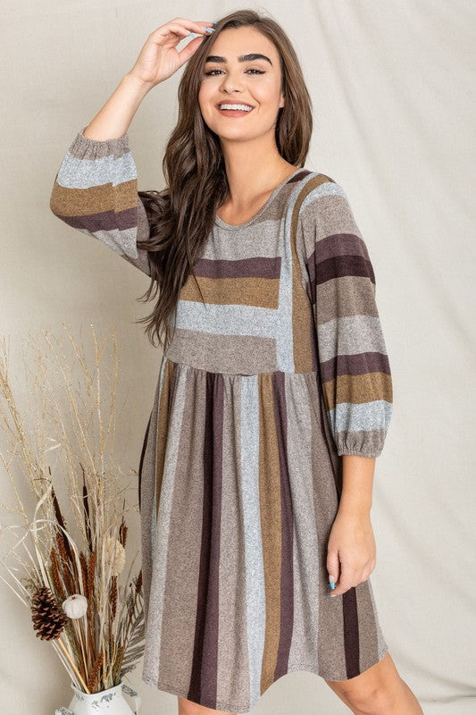 A person stands smiling, dressed in a Mix Stripe Balloon Sleeve Midi Dress that features multi-colored horizontal stripes in shades of blue, brown, and gray. The midi dress, crafted from polyester, includes three-quarter sleeves and handy pockets.