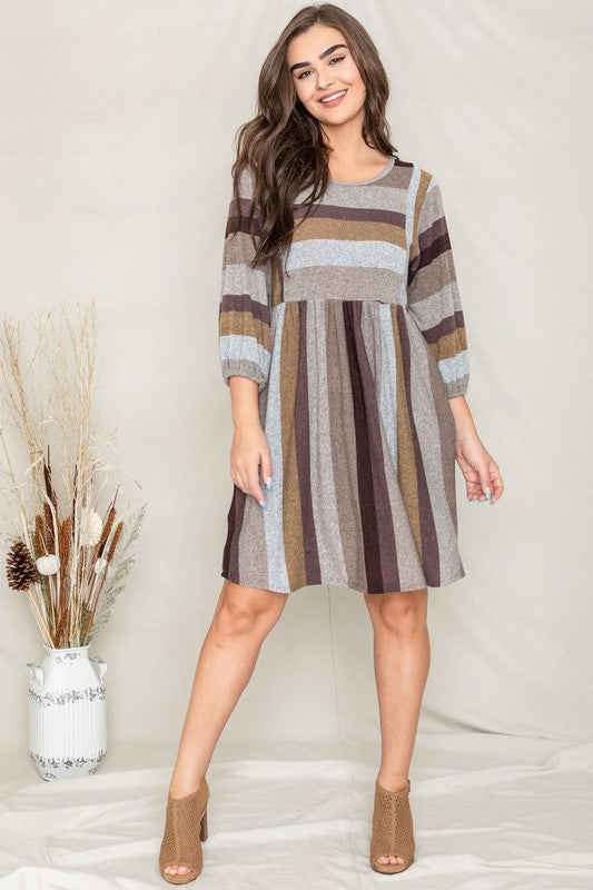 A person stands smiling, dressed in a Mix Stripe Balloon Sleeve Midi Dress that features multi-colored horizontal stripes in shades of blue, brown, and gray. The midi dress, crafted from polyester, includes three-quarter sleeves and handy pockets.