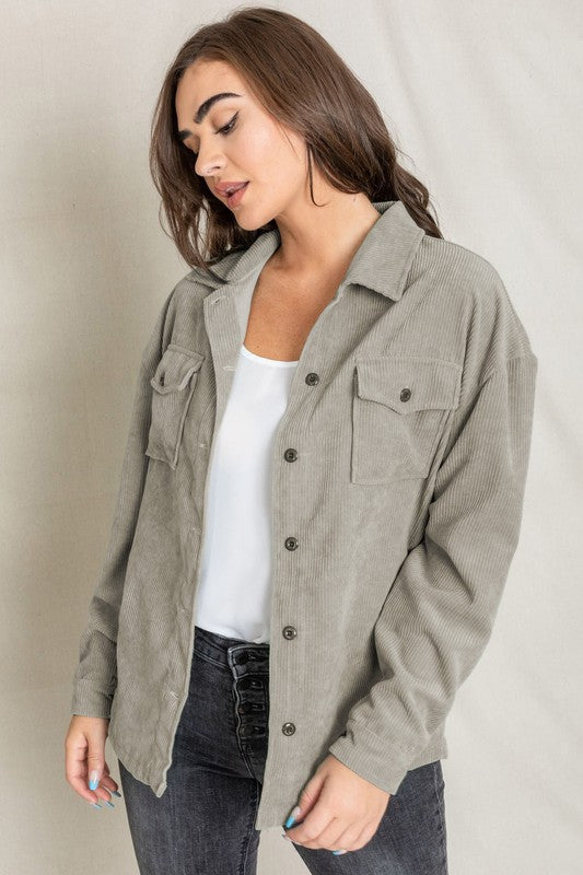 The person is smiling and glancing sideways, dressed in a light gray button-up shirt layered over a white top, exuding an effortlessly stylish vibe. Their outfit mirrors the relaxed elegance of the Corduroy Jacket while delivering a breezier feel for casual comfort.