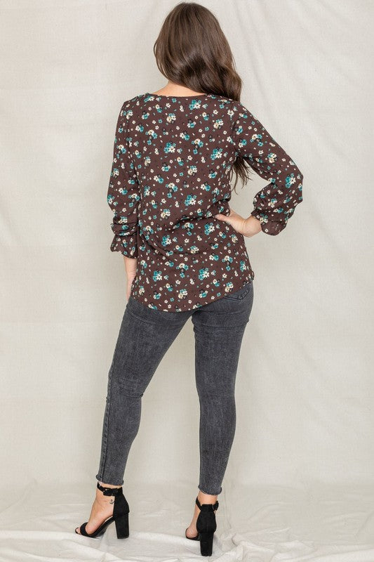 A woman with long brown hair is wearing the Floral Ruffle Sleeve Tunic in mustard yellow, made of 100% polyester, along with dark jeans, standing against a light-colored background.