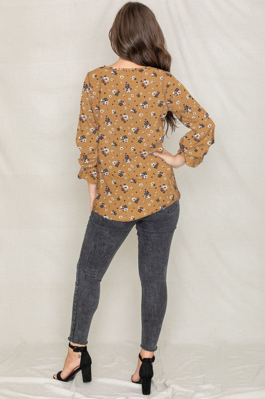 A woman with long brown hair is wearing the Floral Ruffle Sleeve Tunic in mustard yellow, made of 100% polyester, along with dark jeans, standing against a light-colored background.