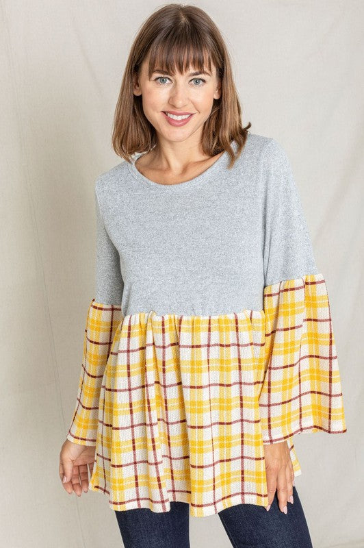 A person wearing the Bell Sleeve Plaid Tunic in gray polyester, featuring yellow plaid flares at the sleeves and bottom hem, is standing against a neutral background.