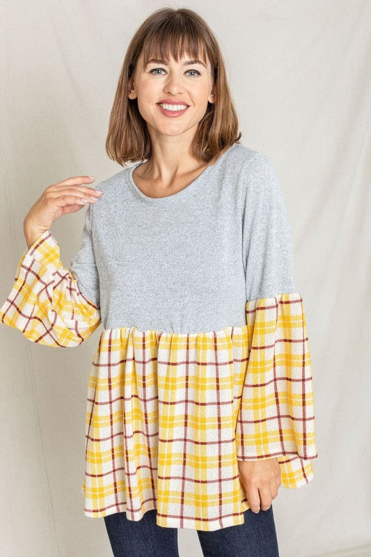 A person wearing the Bell Sleeve Plaid Tunic in gray polyester, featuring yellow plaid flares at the sleeves and bottom hem, is standing against a neutral background.