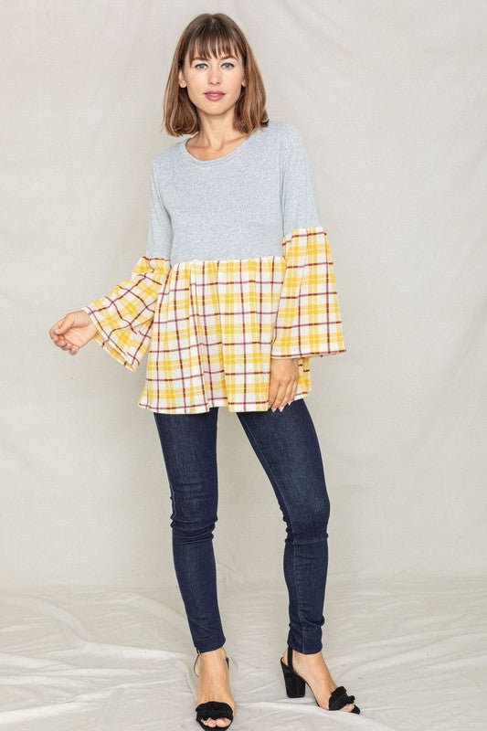 A person wearing the Bell Sleeve Plaid Tunic in gray polyester, featuring yellow plaid flares at the sleeves and bottom hem, is standing against a neutral background.