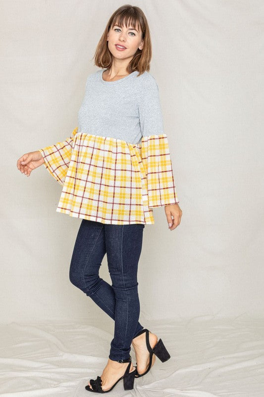 A person wearing the Bell Sleeve Plaid Tunic in gray polyester, featuring yellow plaid flares at the sleeves and bottom hem, is standing against a neutral background.