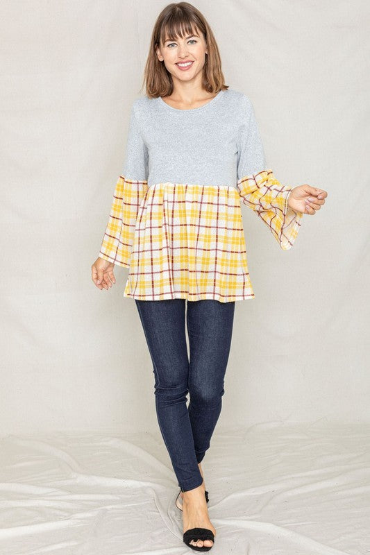 A person wearing the Bell Sleeve Plaid Tunic in gray polyester, featuring yellow plaid flares at the sleeves and bottom hem, is standing against a neutral background.