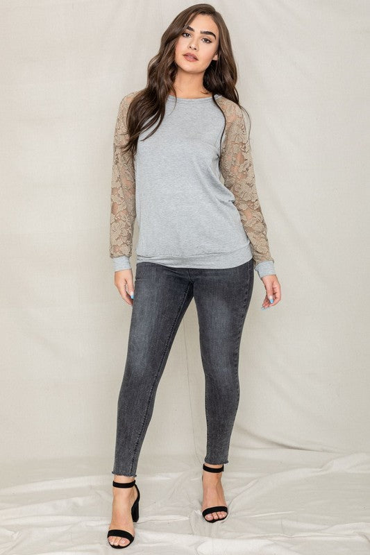 A person in a Plus Lace Sleeve Raglan Tunic, dark jeans, and black heels stands against a plain background.