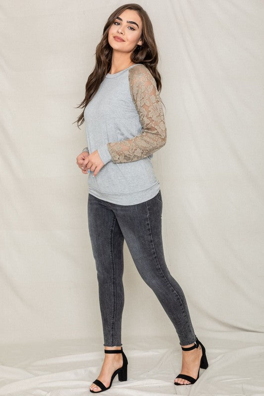 Dressed in a Lace Sleeve Raglan Tunic made from soft rayon spandex fabric, a woman poses elegantly against a plain background, pairing the tunic effortlessly with dark jeans. Made in the United States, her outfit beautifully combines comfort and style.