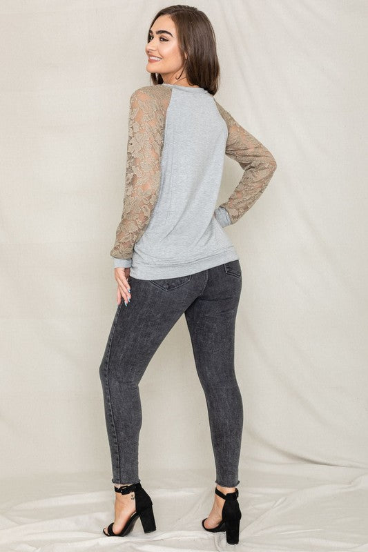 A person in a Plus Lace Sleeve Raglan Tunic, dark jeans, and black heels stands against a plain background.