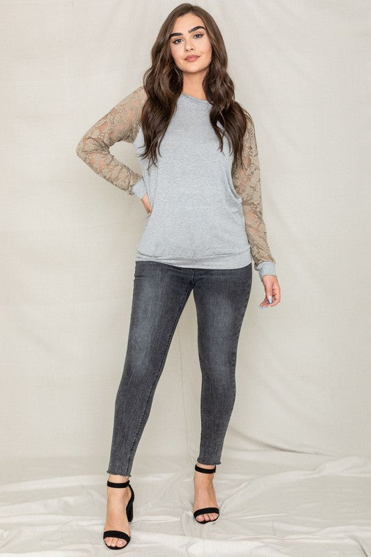 A person in a Plus Lace Sleeve Raglan Tunic, dark jeans, and black heels stands against a plain background.