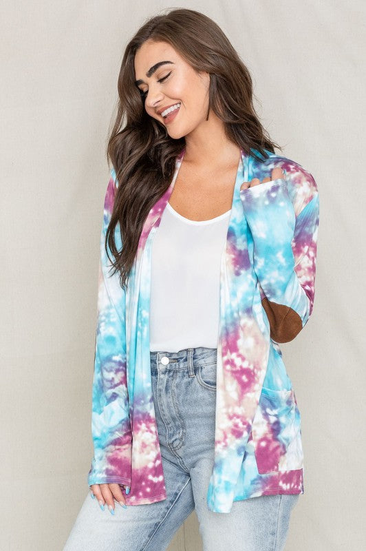 A woman poses for a picture, highlighting her stylish Tie Dye Elbow Patch Open Cardigan. The vibrant colors and unique design emphasize the craftsmanship of this piece, proudly made in the United States.