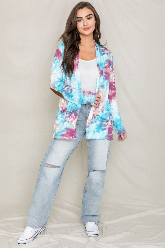 A woman poses for a picture, highlighting her stylish Tie Dye Elbow Patch Open Cardigan. The vibrant colors and unique design emphasize the craftsmanship of this piece, proudly made in the United States.