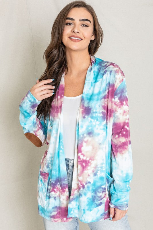 A woman poses for a picture, highlighting her stylish Tie Dye Elbow Patch Open Cardigan. The vibrant colors and unique design emphasize the craftsmanship of this piece, proudly made in the United States.