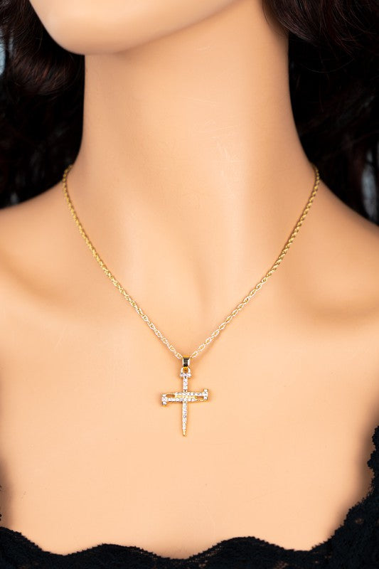 A Nail shape cross pendant necklace with a rope chain, featuring small gemstones, rests elegantly on a marble surface. In the background, an open magazine reveals a tranquil beach scene.