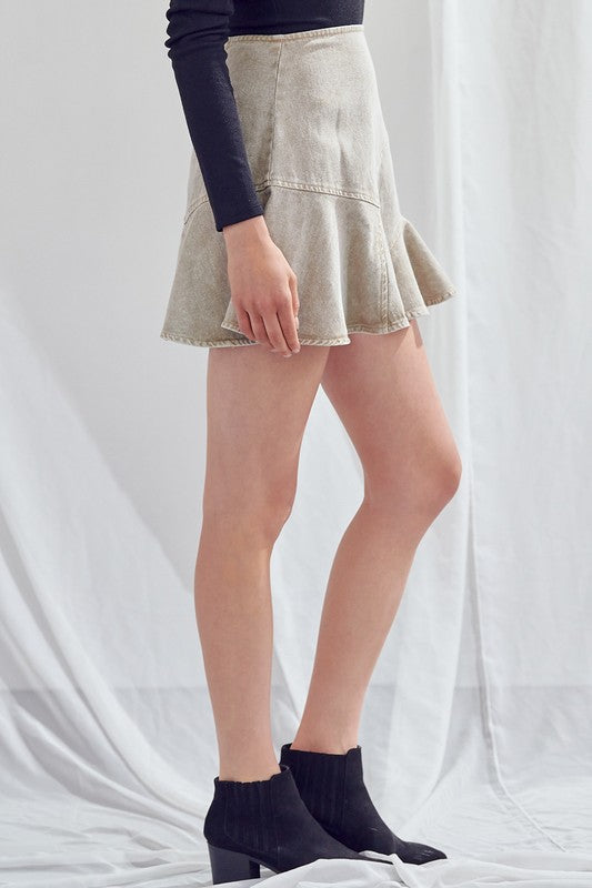 Person wearing a light-colored, acid wash A-Line skirt at mini length, paired with a long-sleeve black top and black ankle boots stands against a white background.