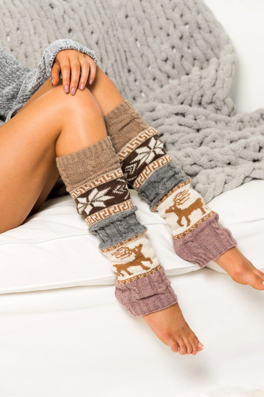 A person wearing Nordic Snowflake Leg Warmers featuring a winter Nordic print sits on a white sofa, their legs extended and crossed.