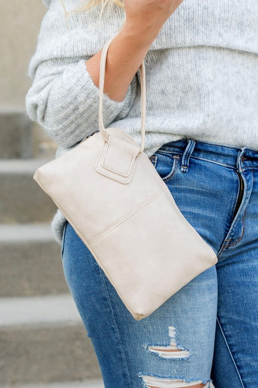 Person in a light sweater and ripped jeans holding a compact size, tan Wristlet Mini Clutch made of vegan PU leather.