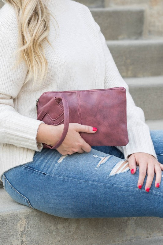 Person in a light sweater and ripped jeans holding a compact size, tan Wristlet Mini Clutch made of vegan PU leather.