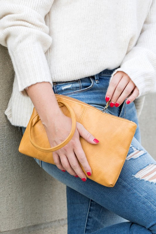 Person in a light sweater and ripped jeans holding a compact size, tan Wristlet Mini Clutch made of vegan PU leather.