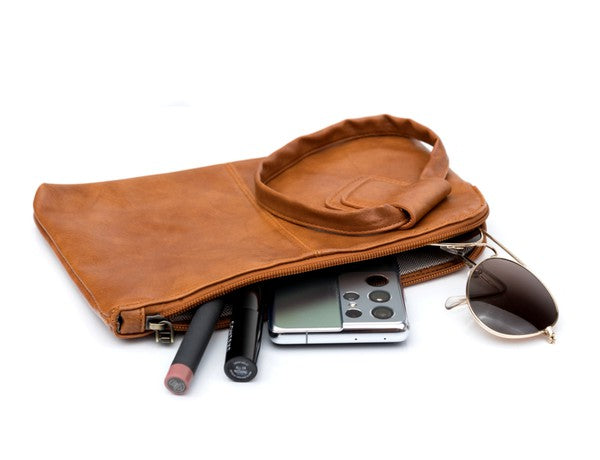 Person in a light sweater and ripped jeans holding a compact size, tan Wristlet Mini Clutch made of vegan PU leather.