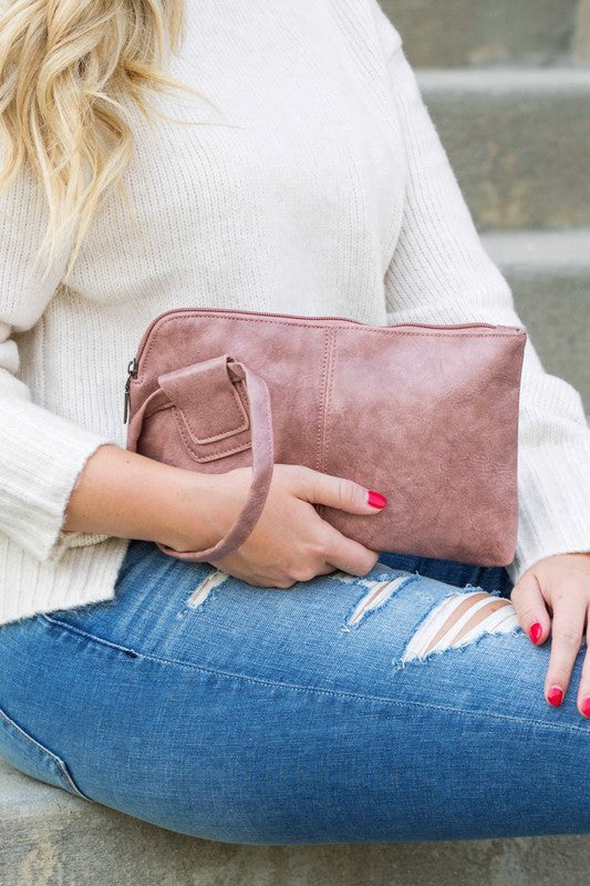 Person in a light sweater and ripped jeans holding a compact size, tan Wristlet Mini Clutch made of vegan PU leather.